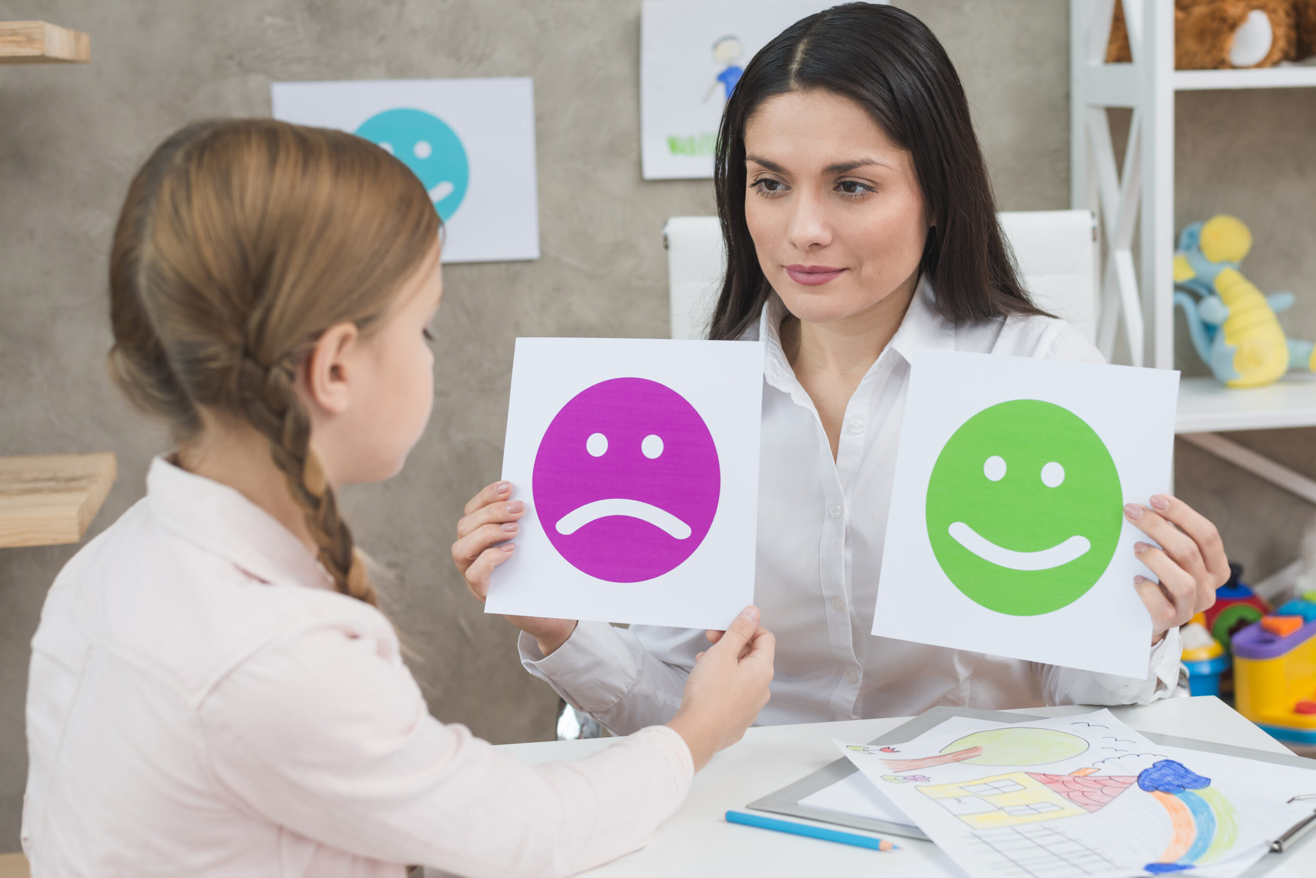 close-up-girl-choosing-sad-face-emoticons-paper-held-by-smiling-young-psychologist